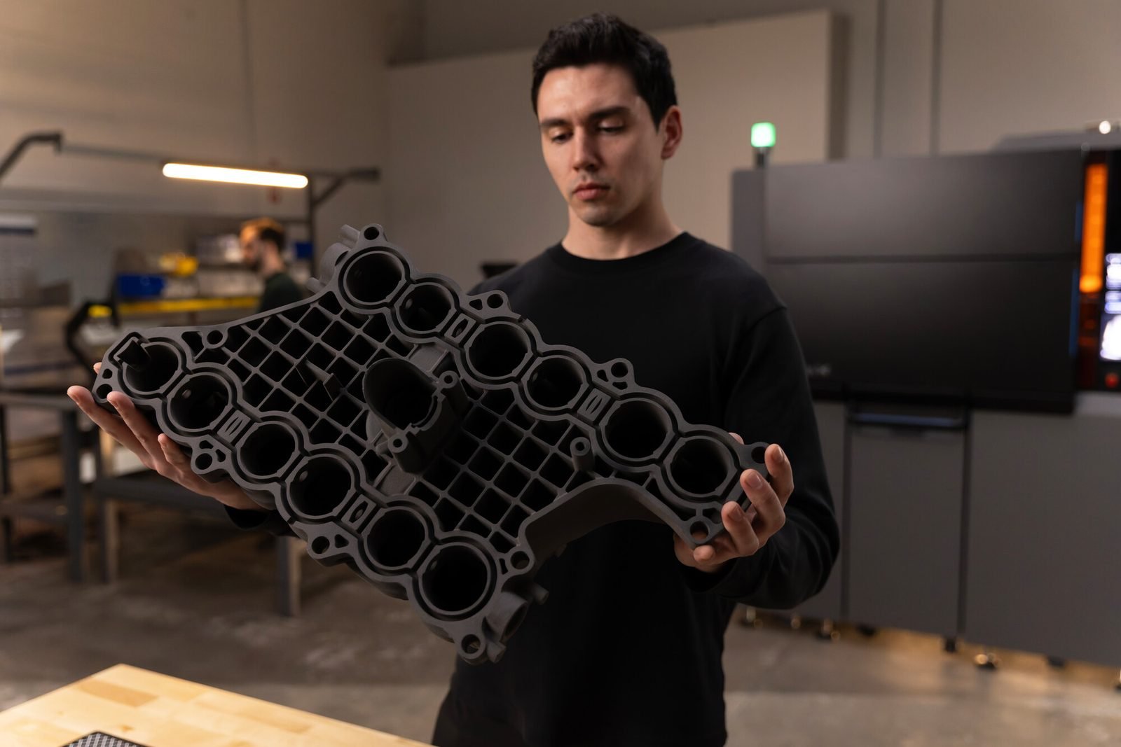 Un ingeniero sostiene un múltiple de admisión impreso en SLS en el taller